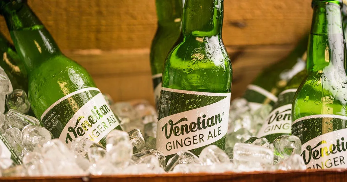 Green glass bottles of Venetian Ginger Ale packed in ice in a wooden crate, labels facing out.