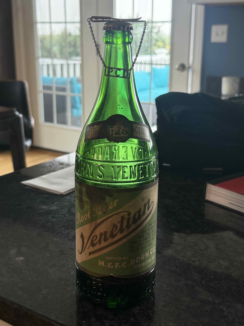 Embossed green glass bottle with a Venetian Root Beer label, bottled by M. & F.C. Dorn Co., Burlington VT, with a monogrammed tie clip resting on the neck