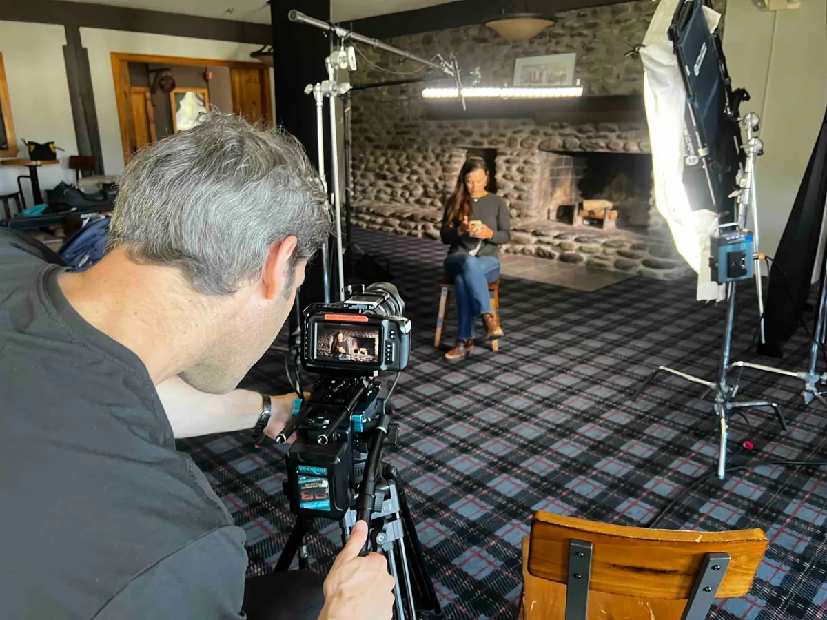 An interview beside a large stone fireplace in a lodge, camera operator framing the shot.