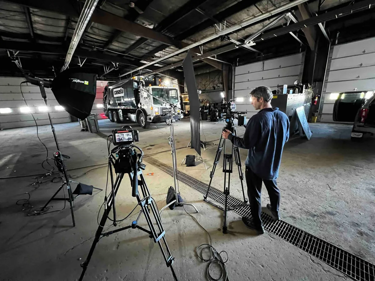 Two cameras and softboxes set up in a fleet garage in front of a Casella refuse truck.