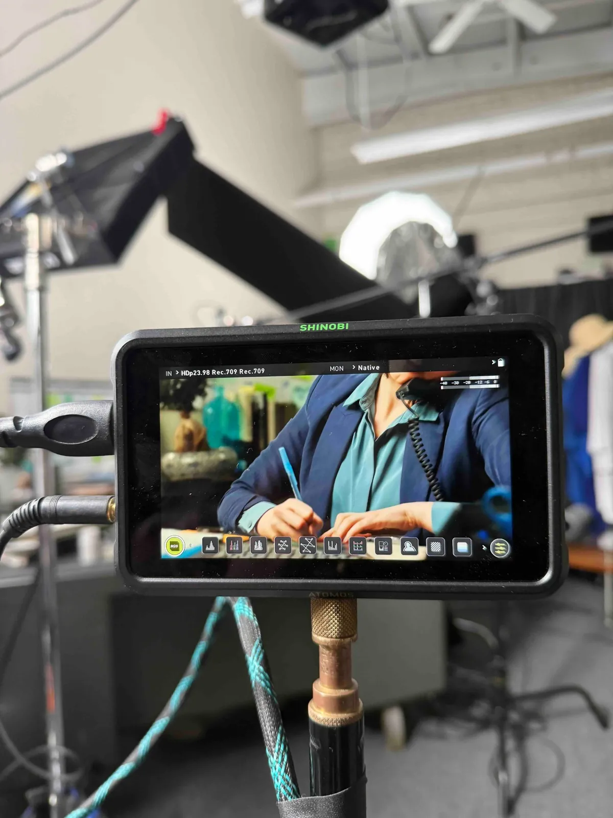 A camera monitor showing a framed shot of a subject at a desk, the lit set visible out of focus behind it.