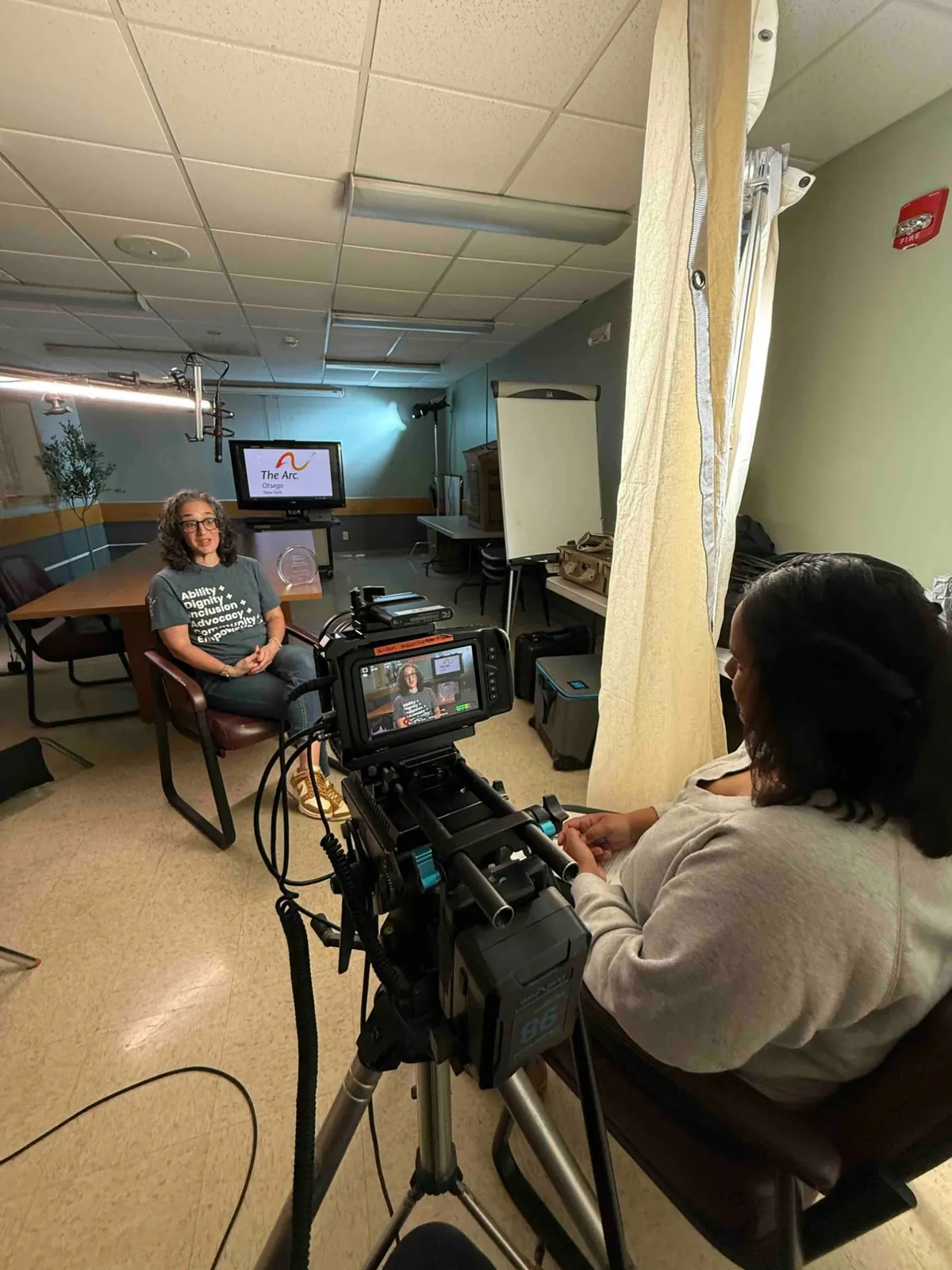 A nonprofit staff member being interviewed in a meeting room, monitor showing the framing.