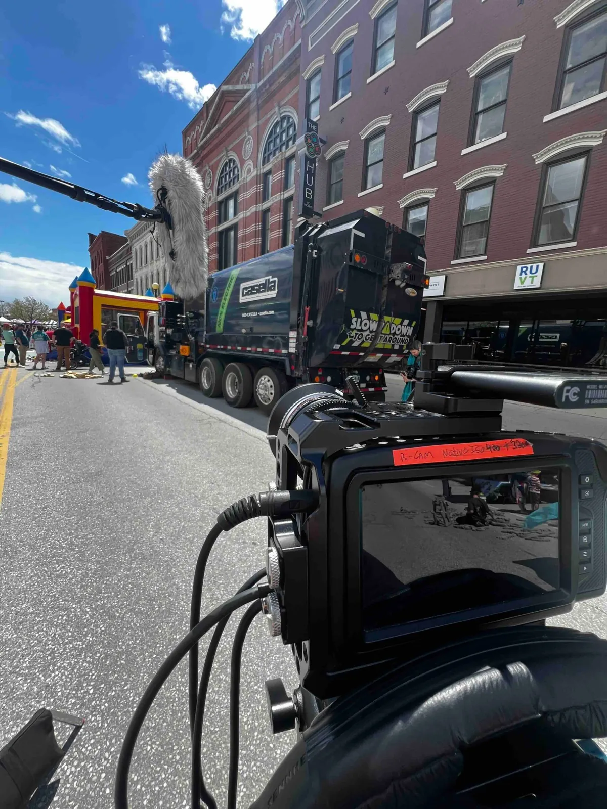 A boom microphone and camera covering a street festival with an electric refuse truck in shot.