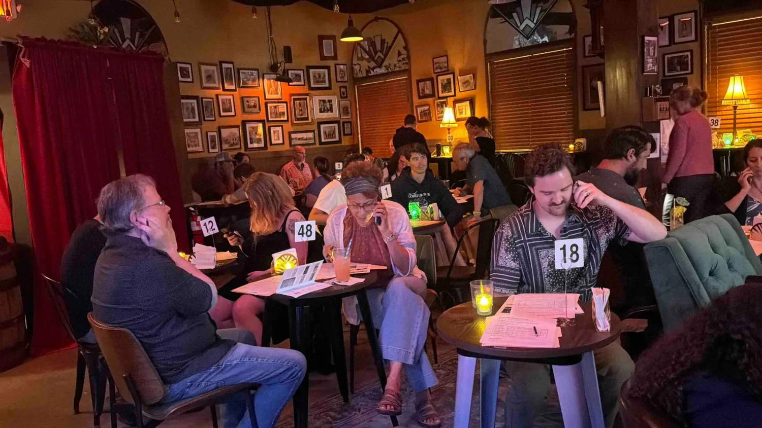 Guests at Venetian Soda Lounge holding telephone handsets to their ears while reading printed case files during Who Killed Dr. Funk?